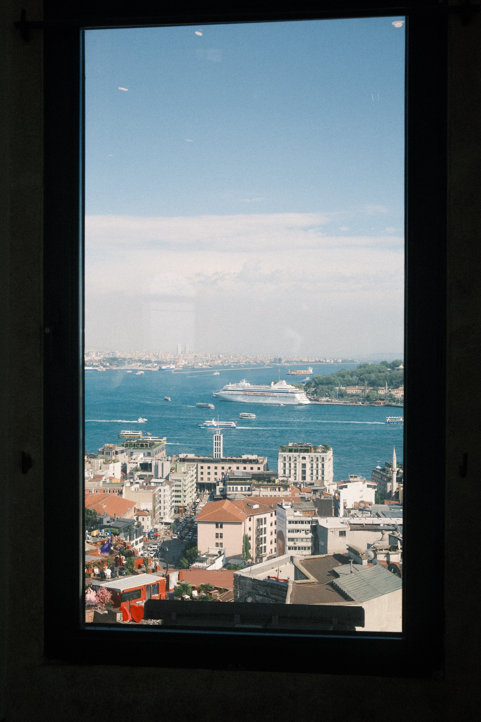 The Bosphorus and Istanbul's rooftops seen through a window, a cruise ship and ferries crossing the strait.