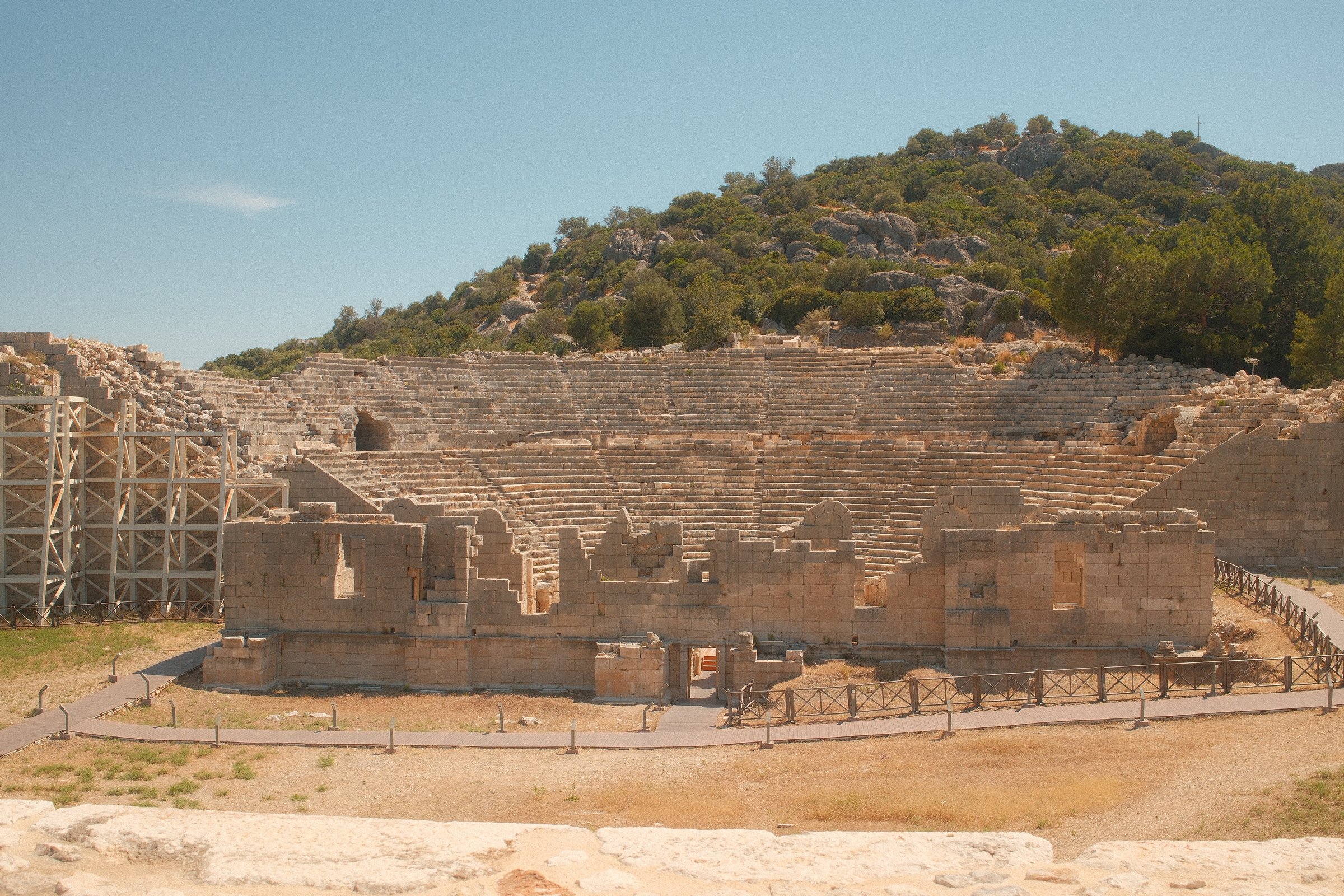 The tiered stone seating of an ancient amphitheater built into a wooded hillside.